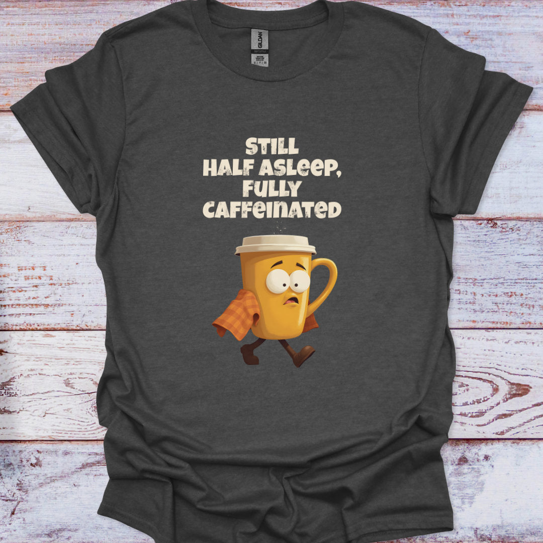 Dark gray t-shirt with a cartoon coffee mug and text 'Still half asleep, fully caffeinated' on a wooden surface.