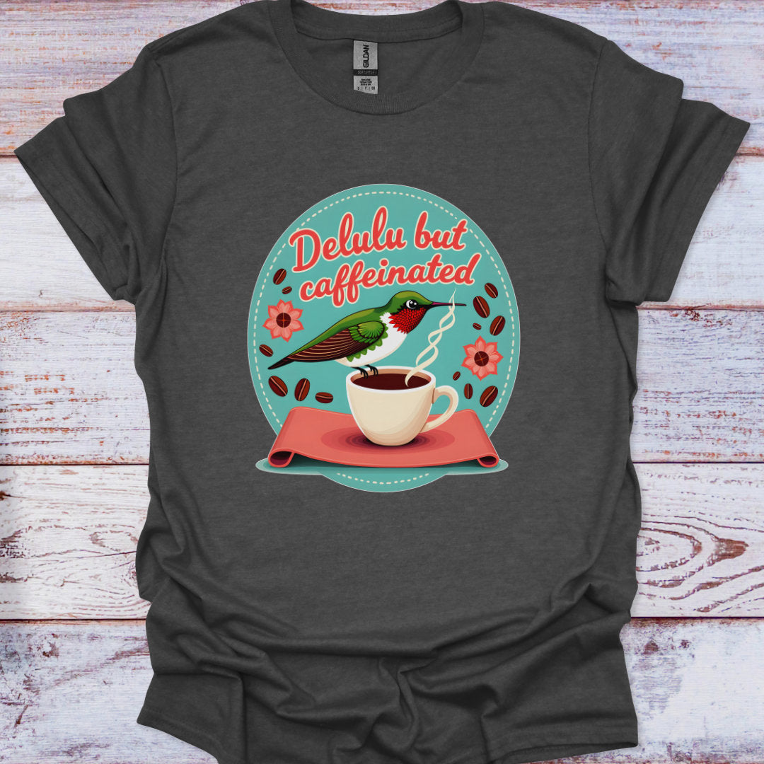 Dark gray t-shirt with a graphic of a bird drinking from a coffee cup and text 'Delulu but caffeinated' on a wooden surface.