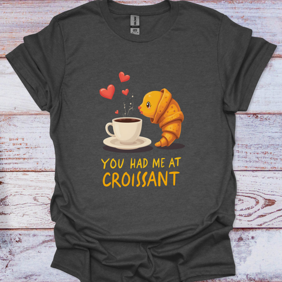 Dark gray t-shirt with a cartoon croissant and coffee cup graphic and text 'You Had Me at Croissant' on a wooden surface.