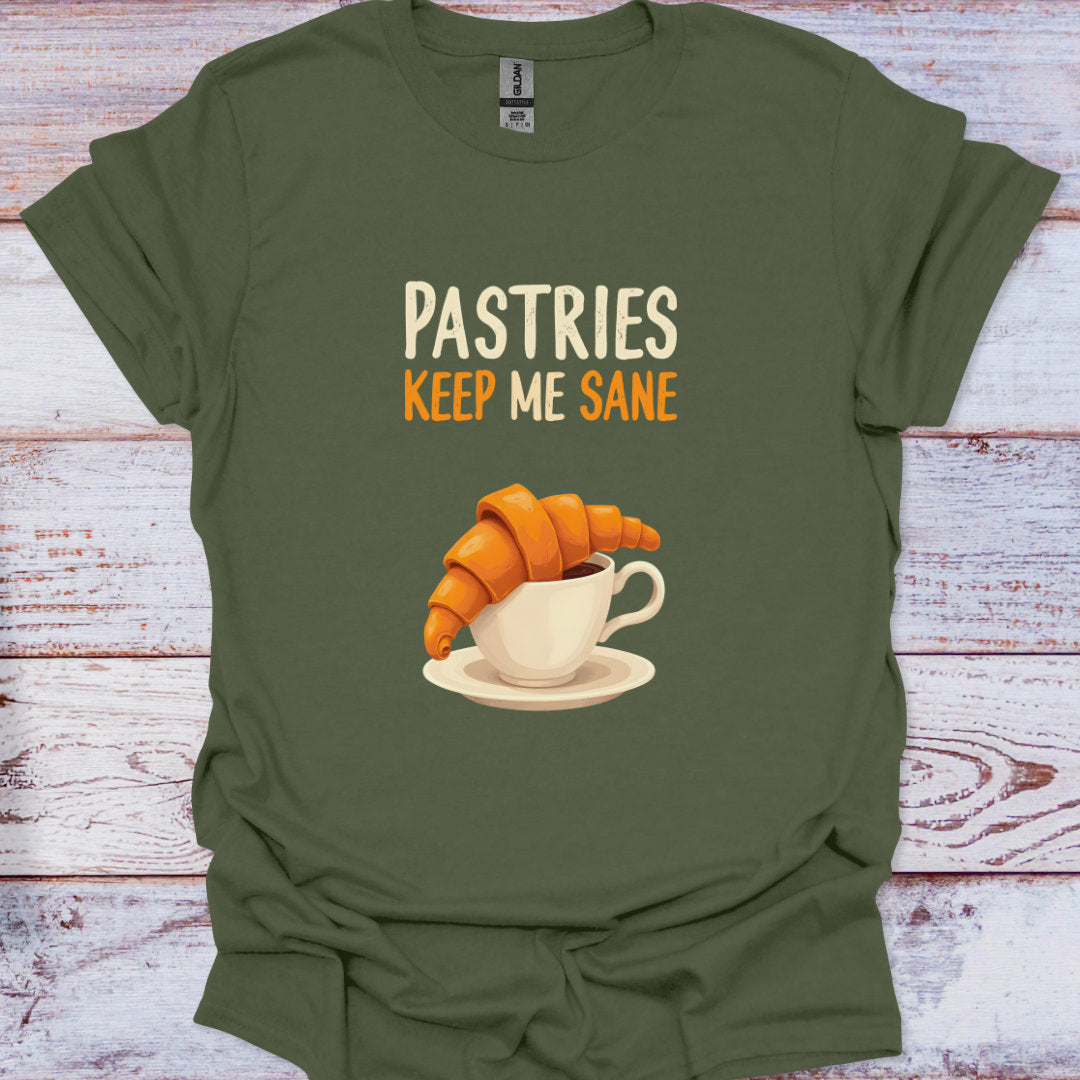 Green t-shirt with a graphic of a croissant and coffee cup and text 'Pastries Keep Me Sane' on a wooden surface.