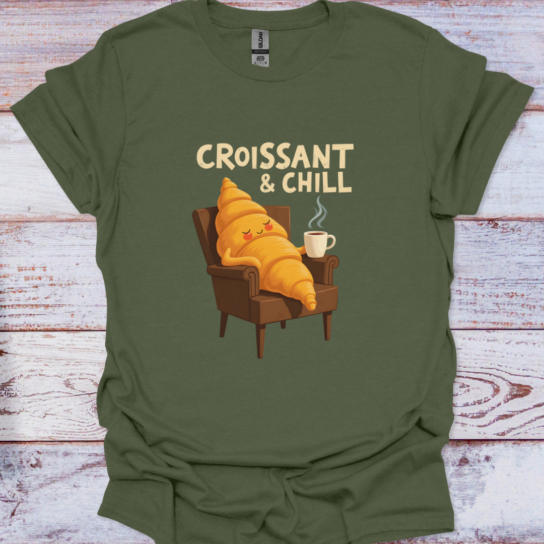 Green t-shirt with a cartoon croissant character and 'Croissant & Chill' text on a wooden surface