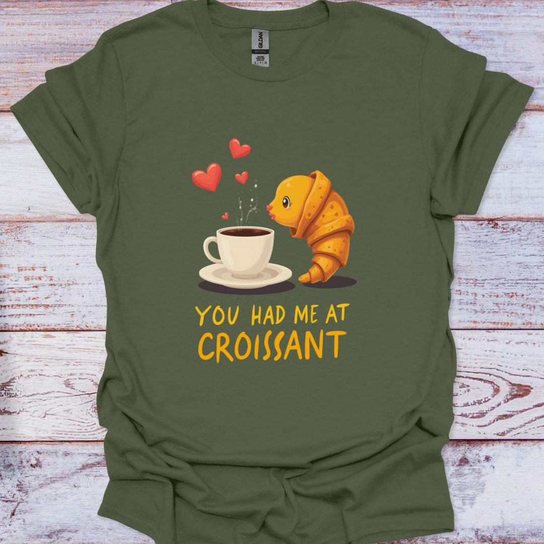 Green t-shirt with a cartoon croissant and coffee cup design on a wooden surface
