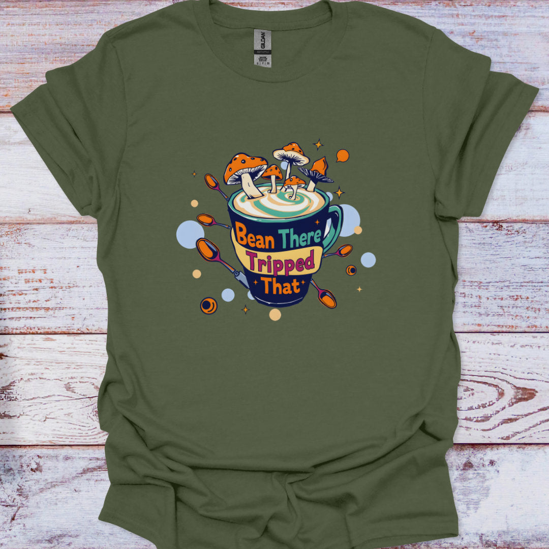 Green t-shirt with a graphic design of a coffee cup and text 'Bean There, Tripped That' on a wooden surface.