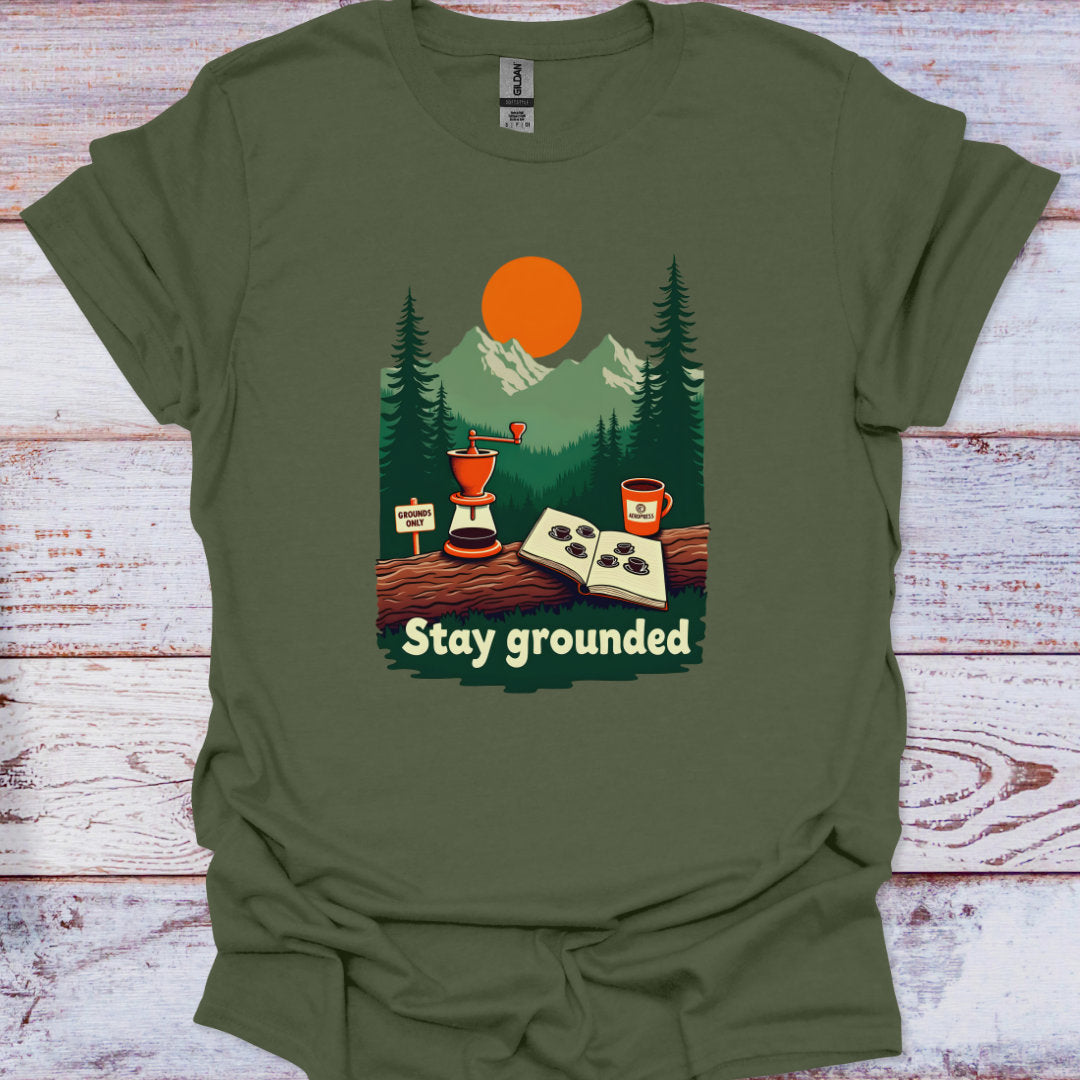 Green t-shirt with a nature-themed graphic and 'Stay grounded' text on a wooden surface