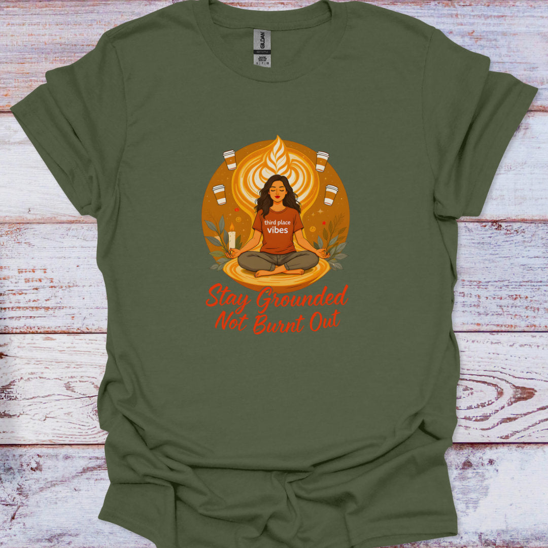 Green t-shirt with a graphic of a woman meditating and text 'Stay Grounded Not Burnt Out' on a wooden surface.