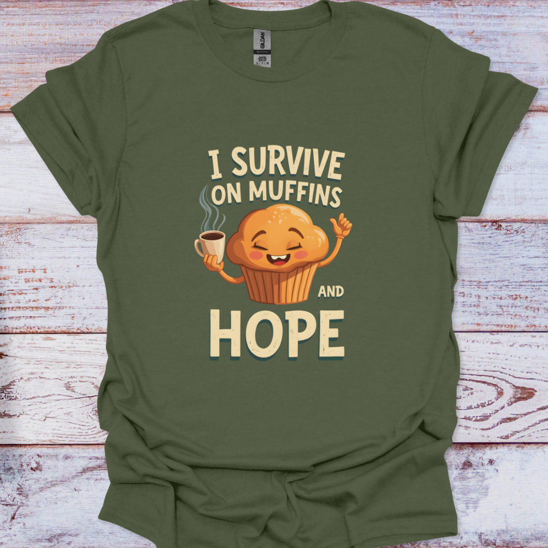 Green t-shirt with a muffin graphic and text 'I survive on muffins and hope' on a wooden surface.