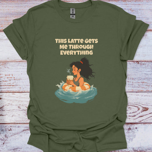 Green t-shirt with a graphic of a woman holding a coffee cup and text 'This Latte Gets Me Through Everything' on a wooden surface.