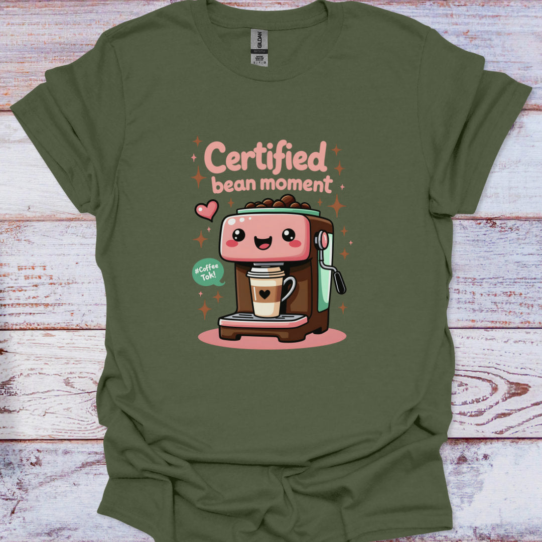 Green t-shirt with a cartoon coffee machine and text 'Certified bean moment' on a wooden surface.