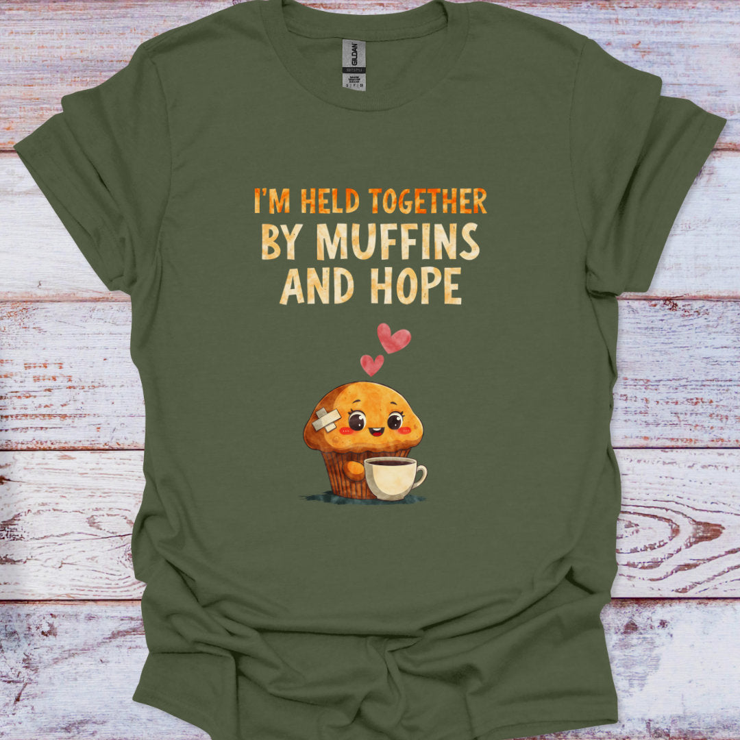 Green t-shirt with a cartoon muffin and text 'I'm held together by muffins and hope' on a wooden surface.
