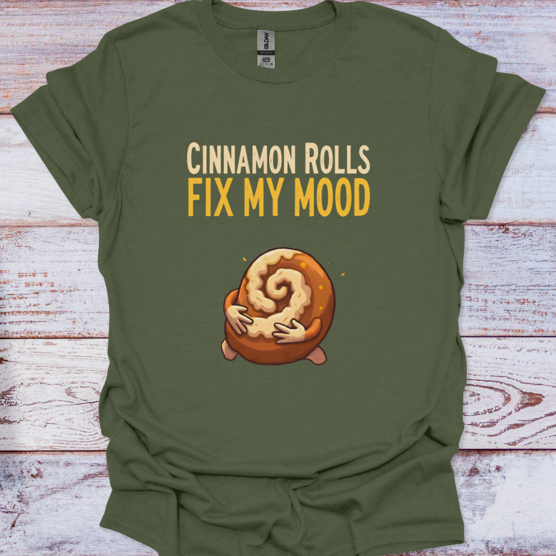 Green t-shirt with cinnamon roll graphic and text 'Cinnamon Rolls Fix My Mood' on a wooden surface