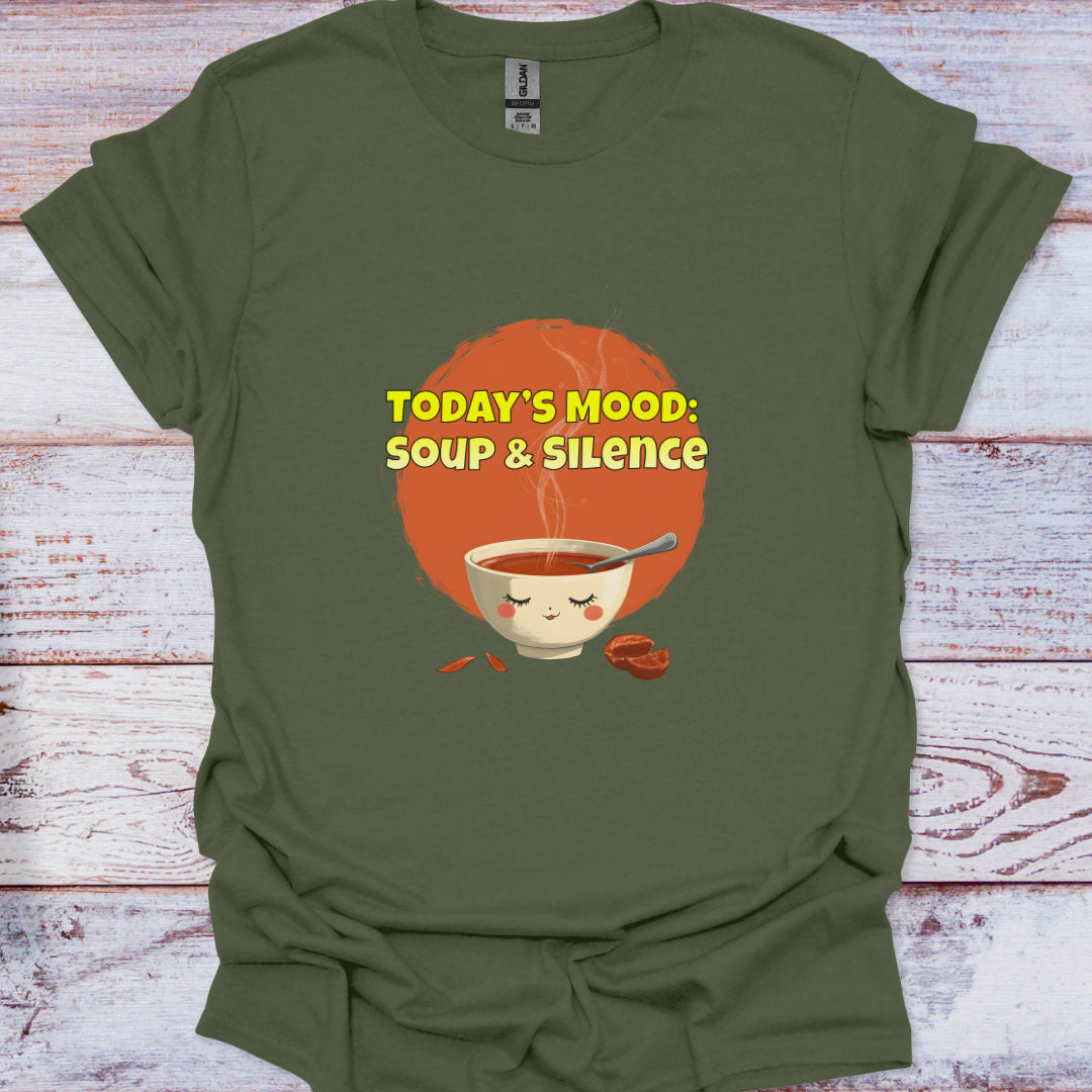 Green t-shirt with a graphic of a bowl of soup and text 'TODAY'S MOOD: SOUP & SILENCE' on a wooden surface.