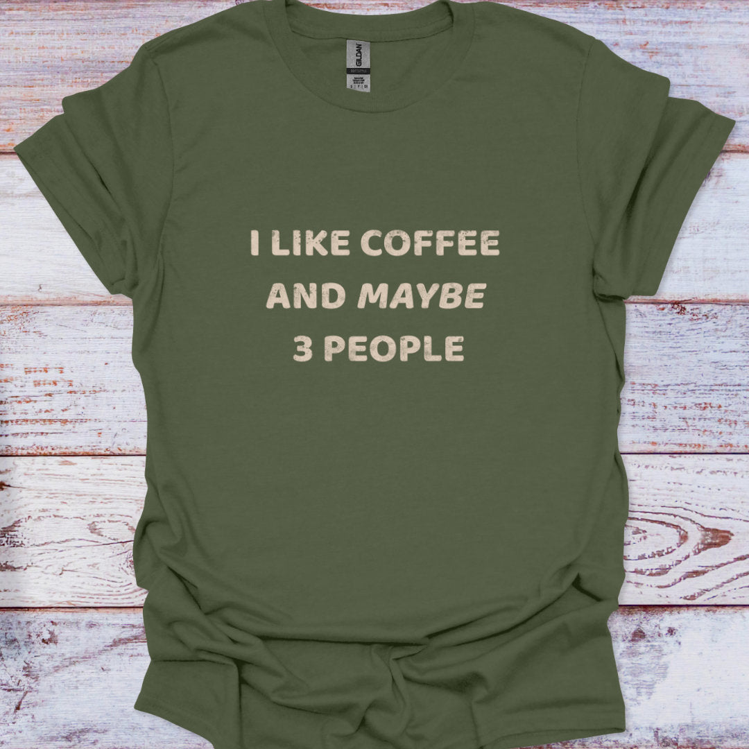 Green t-shirt with text 'I LIKE COFFEE AND MAYBE 3 PEOPLE' on a wooden surface