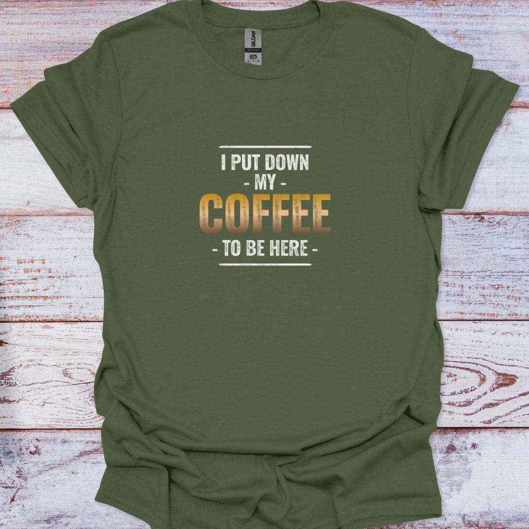 "I Put Down My Coffee To Be Here" humorous graphic in distressed fonts on a military green t-shirt.