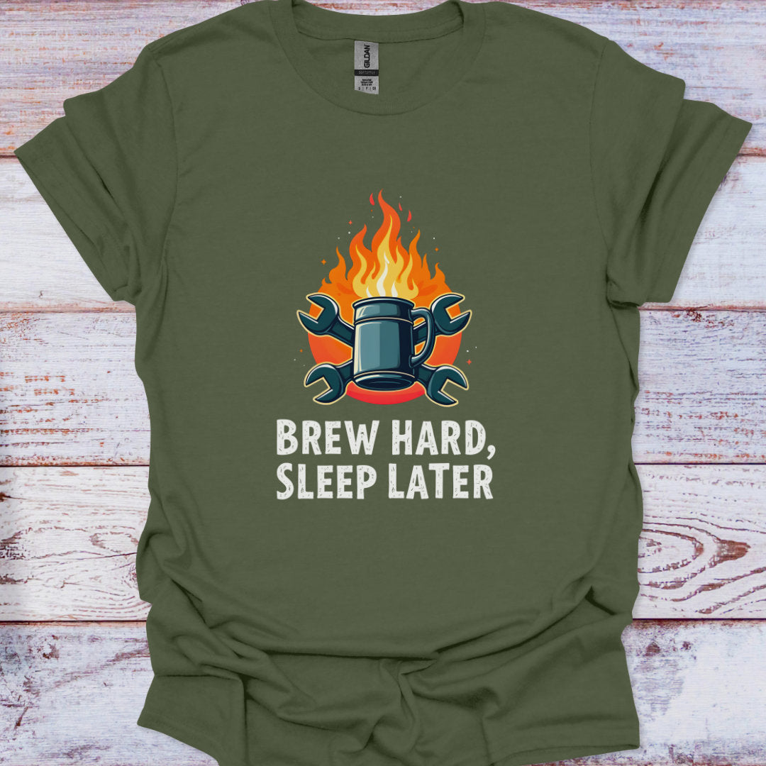 Green t-shirt with a graphic of a mug on fire and the text 'Brew Hard, Sleep Later' on a wooden surface.