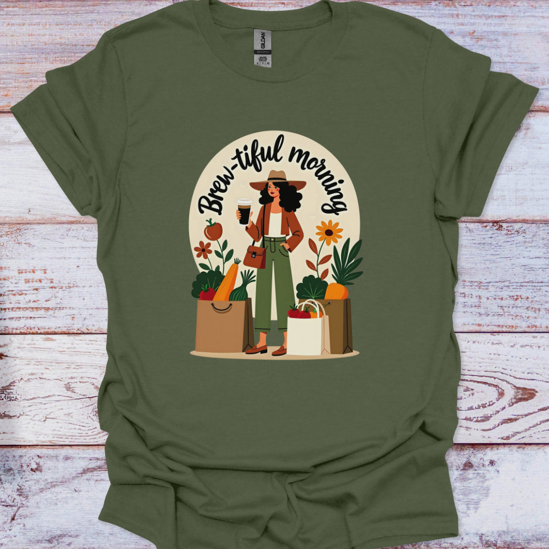 Green t-shirt with a graphic of a woman holding a coffee cup and shopping bags, with 'Brew-iful morning' text, on a wooden surface.