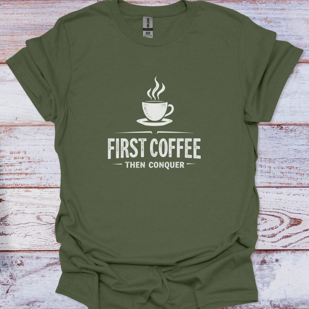 Green t-shirt with a coffee cup graphic and text 'First Coffee Then Conquer' on a wooden surface.