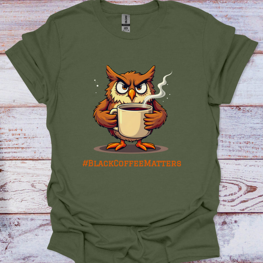Green t-shirt with an owl holding a coffee cup and '#BLACKCOFFEEMATTERS' text on a wooden surface.