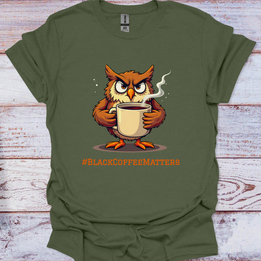 Green t-shirt with an owl holding a coffee cup and '#BLACKCOFFEEMATTERS' text on a wooden surface.