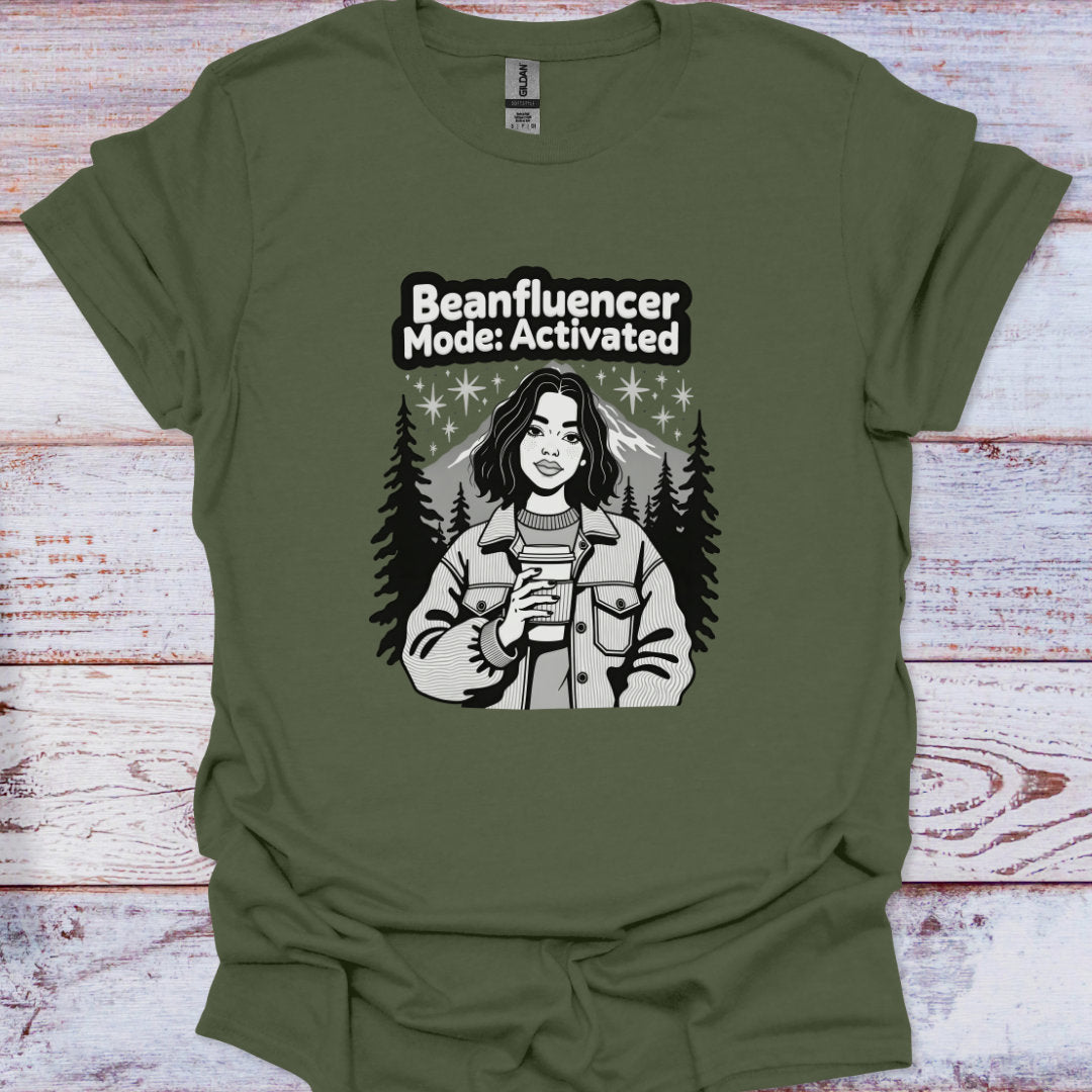 Green t-shirt with a graphic of a person holding a coffee cup and text 'Beanfluencer Mode: Activated' on a wooden surface.