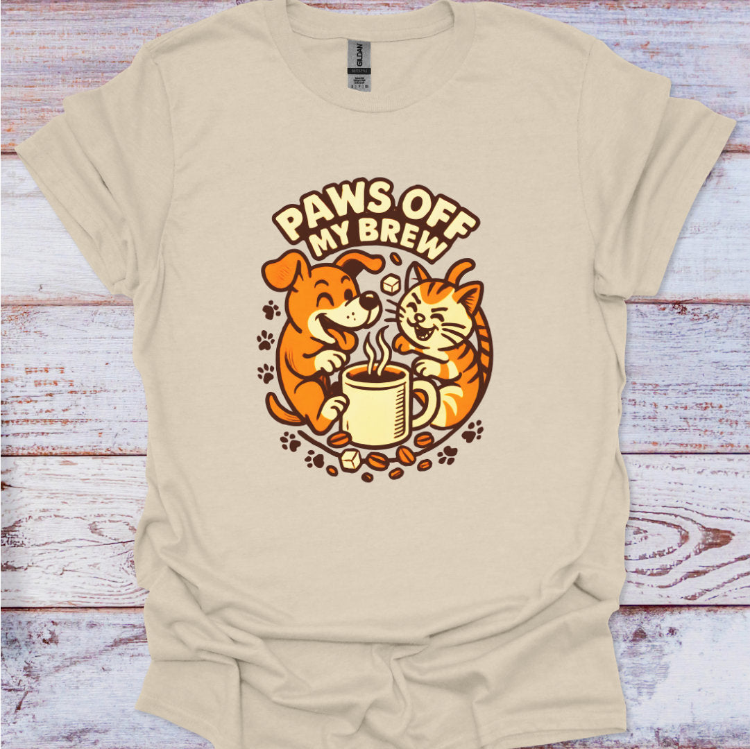 Beige t-shirt with a graphic of a dog and cat drinking coffee and 'Paws Off My Brew' text on a wooden surface.