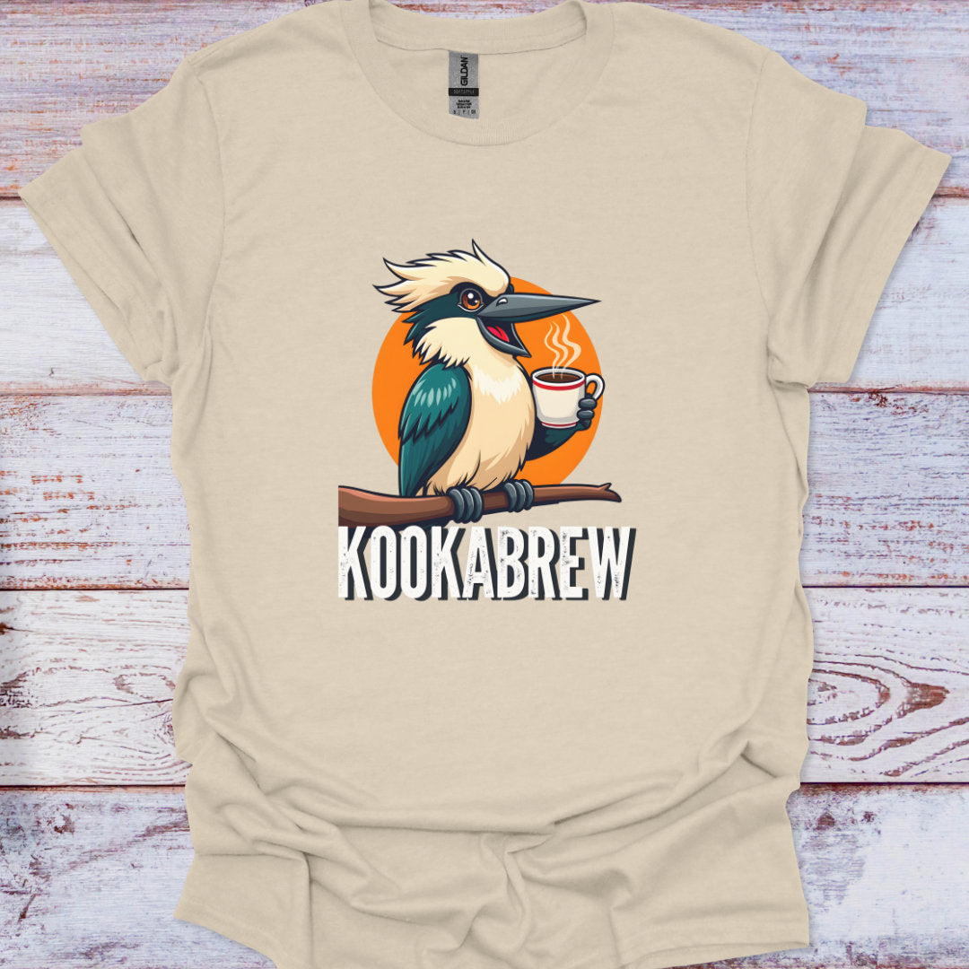 Beige t-shirt with a cartoon kookaburra holding a coffee cup and 'Kookabrew' text on a wooden surface.