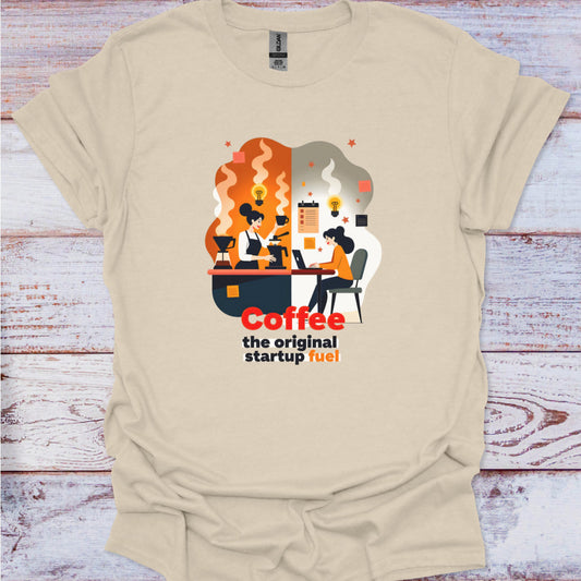 Beige t-shirt with a graphic design of people working at a desk with coffee cups, and text 'Coffee the original startup fuel' on a wooden surface.
