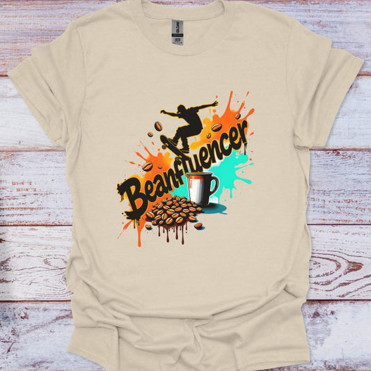 Beige t-shirt with a graphic design featuring coffee beans, a cup, and the word 'Beanfluencer' on a wooden surface.