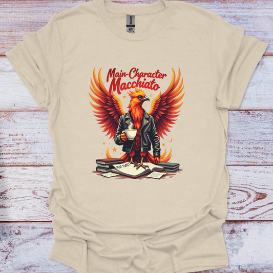 Beige t-shirt with a graphic of an eagle holding a cup and text 'Main Character Macchiato' on a wooden surface.