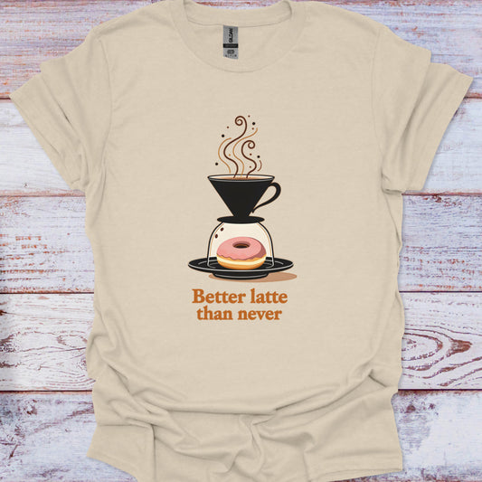 Beige t-shirt with a coffee-themed graphic and text 'Better latte than never' on a wooden surface.