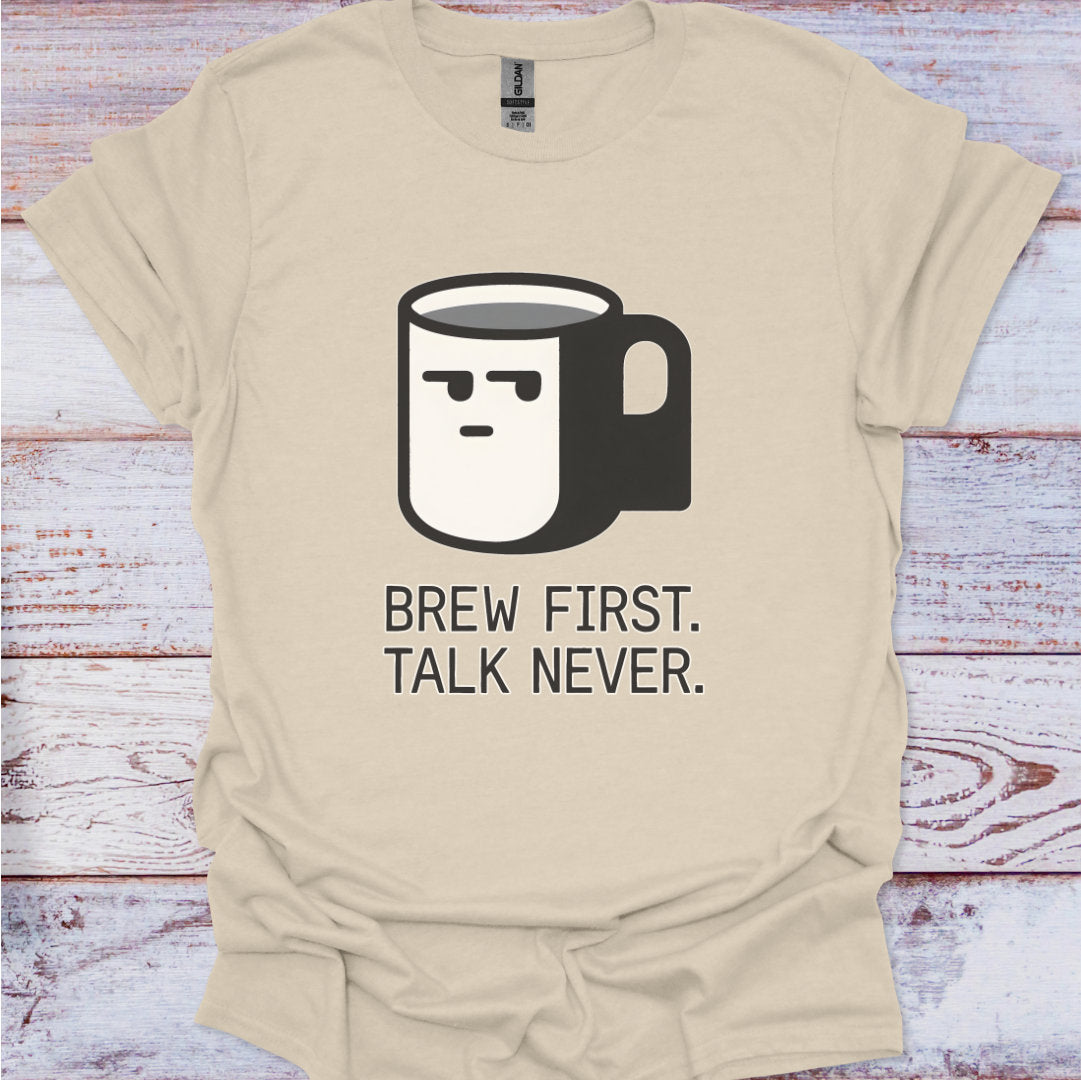 Beige t-shirt with a coffee mug graphic and text 'Brew First. Talk Never.' on a wooden surface.