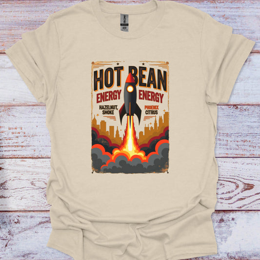 Beige t-shirt with a graphic design of a rocket and 'Hot Bean Energy' text on a wooden surface.