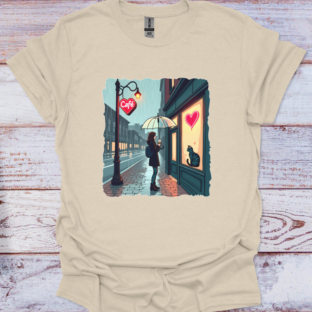 Beige t-shirt with a graphic of a person at a cafe entrance with a heart above, on a wooden surface.