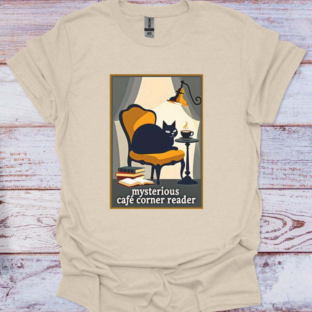 Beige t-shirt with a graphic of a cat in a cafe corner reading a book, on a wooden surface.