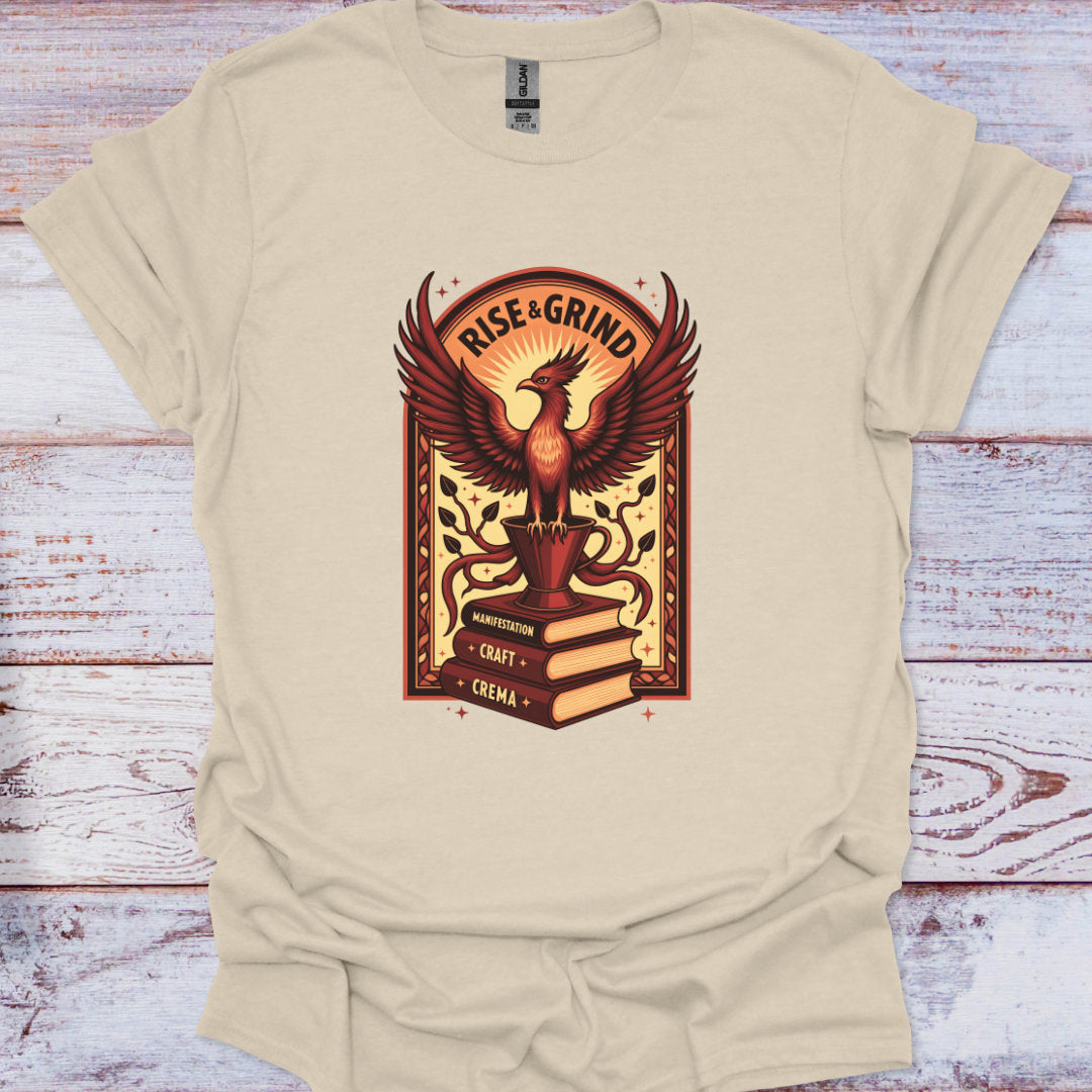 Beige t-shirt with a phoenix graphic and 'Rise & Grind' text on a wooden surface