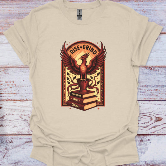 Beige t-shirt with a phoenix graphic and 'Rise & Grind' text on a wooden surface