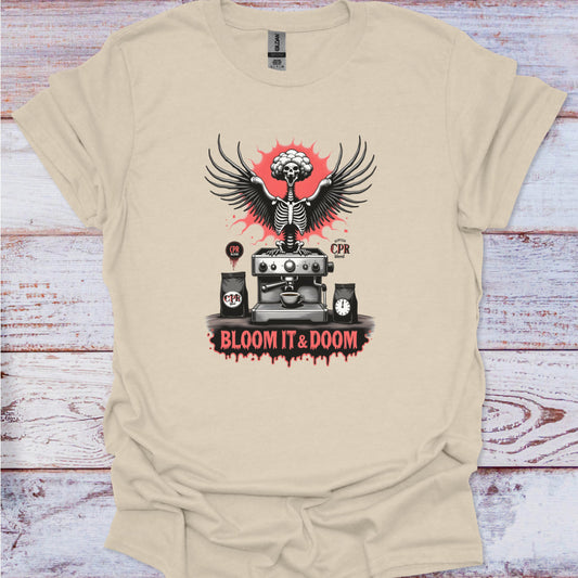 Beige t-shirt with a graphic design featuring a skeleton, coffee machine, and text on a wooden surface.