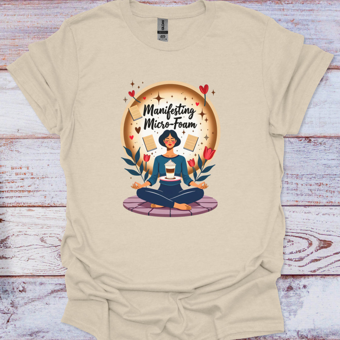 Beige t-shirt with a graphic of a person meditating and text 'Manifesting Micro-Foam' on a wooden surface.