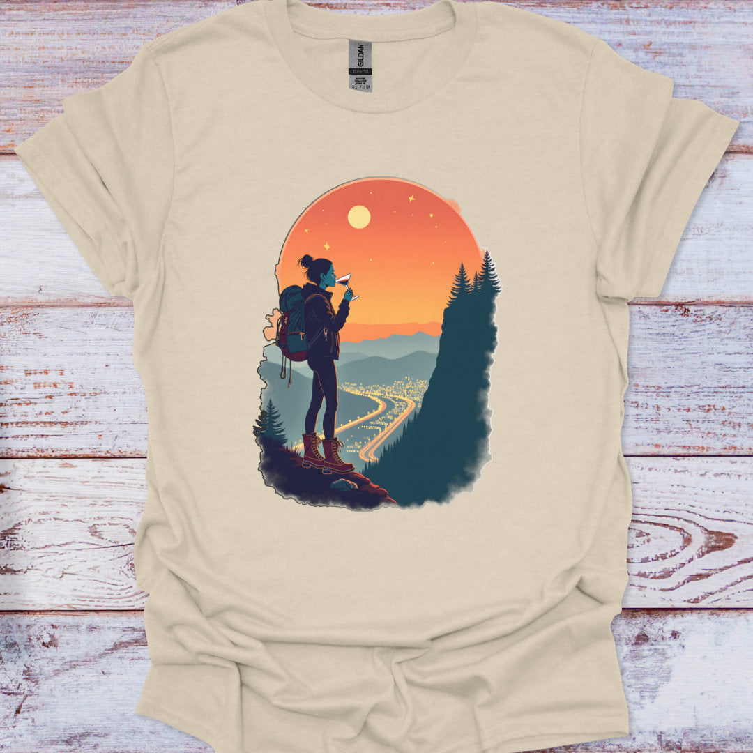 Beige t-shirt with a graphic of a person hiking and a sunset landscape on a wooden surface.