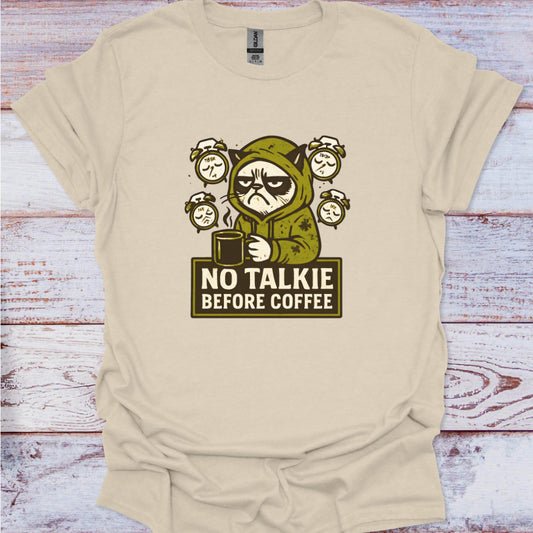 Beige t-shirt with a graphic of a cat in a coffee cup and 'No Talkie Before Coffee' text on a wooden surface.
