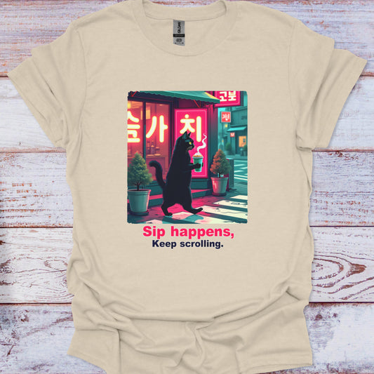 Beige t-shirt with a graphic of a cat in a black coat and text 'Sip happens, Keep scrolling.' on a wooden surface.