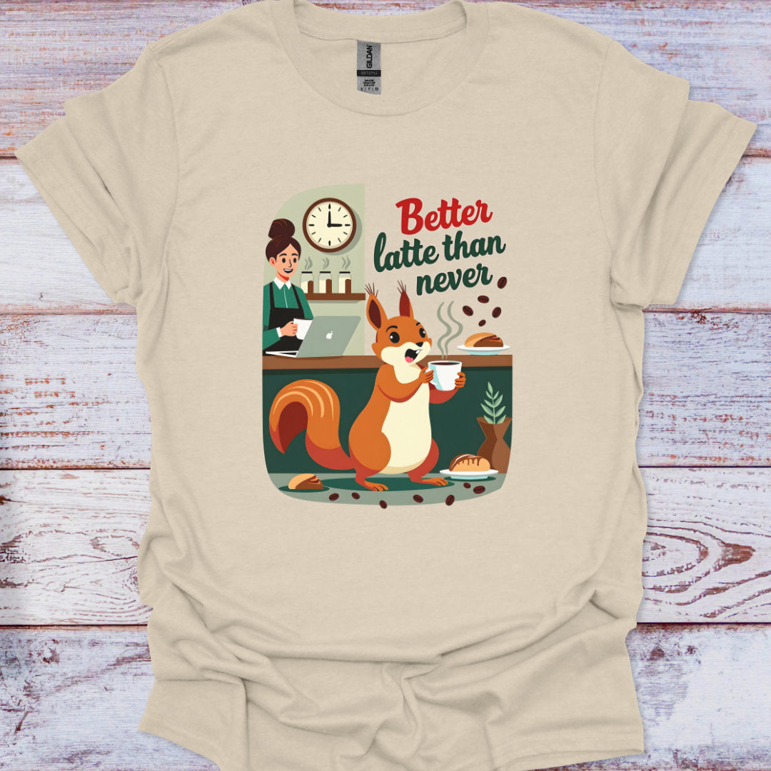 Beige t-shirt with a graphic of a squirrel drinking coffee and text 'Better latte than never' on a wooden surface.