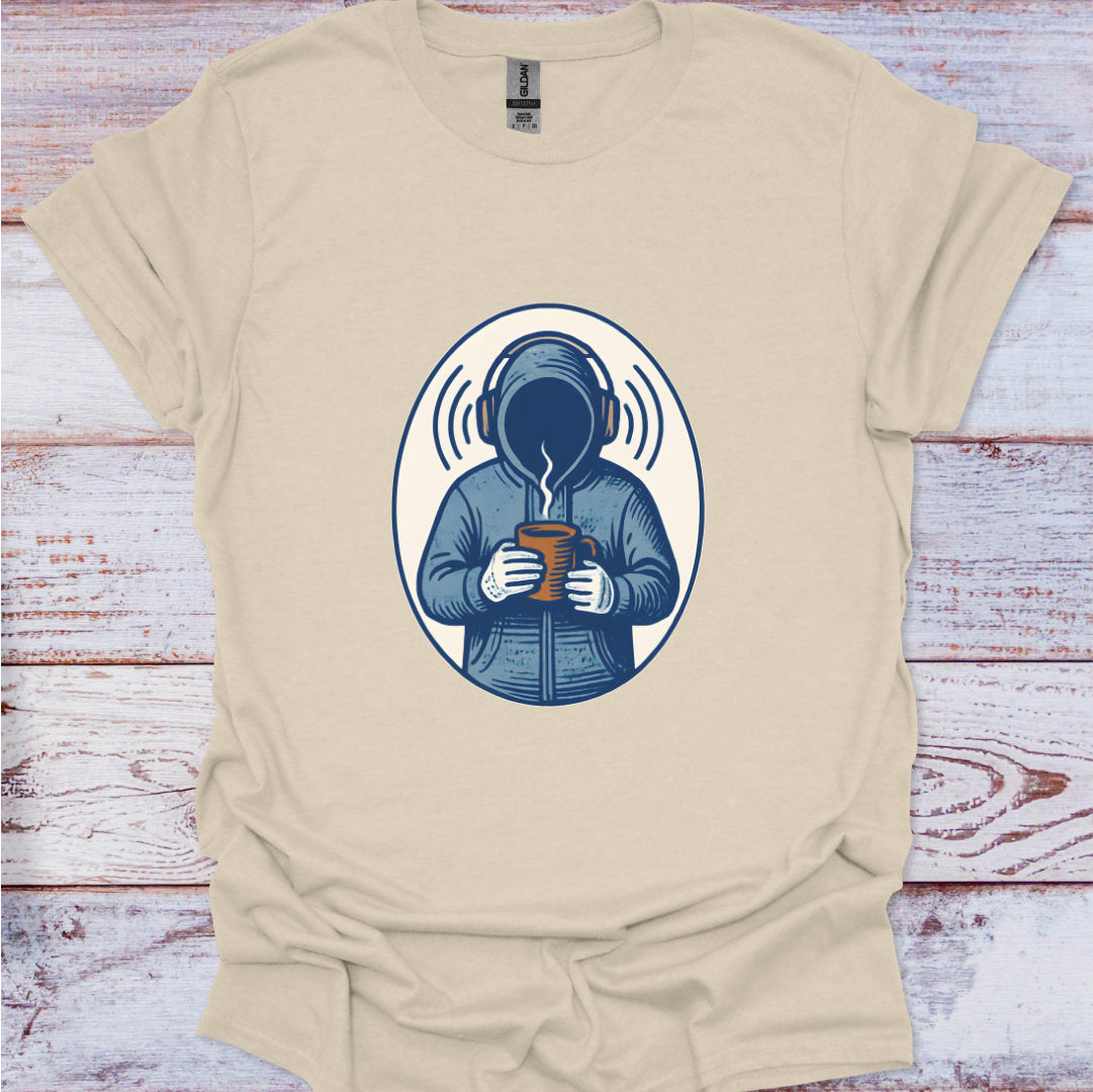 Beige t-shirt with a graphic of a person in a coat holding a mug, on a wooden surface.