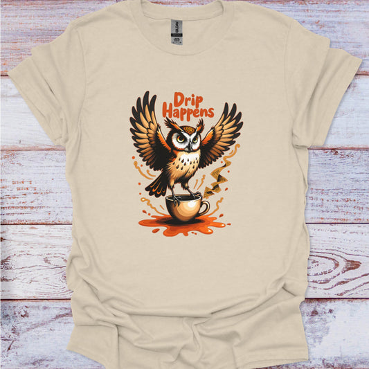 Beige t-shirt with an owl holding a coffee cup and 'Drip Happens' text on a wooden surface