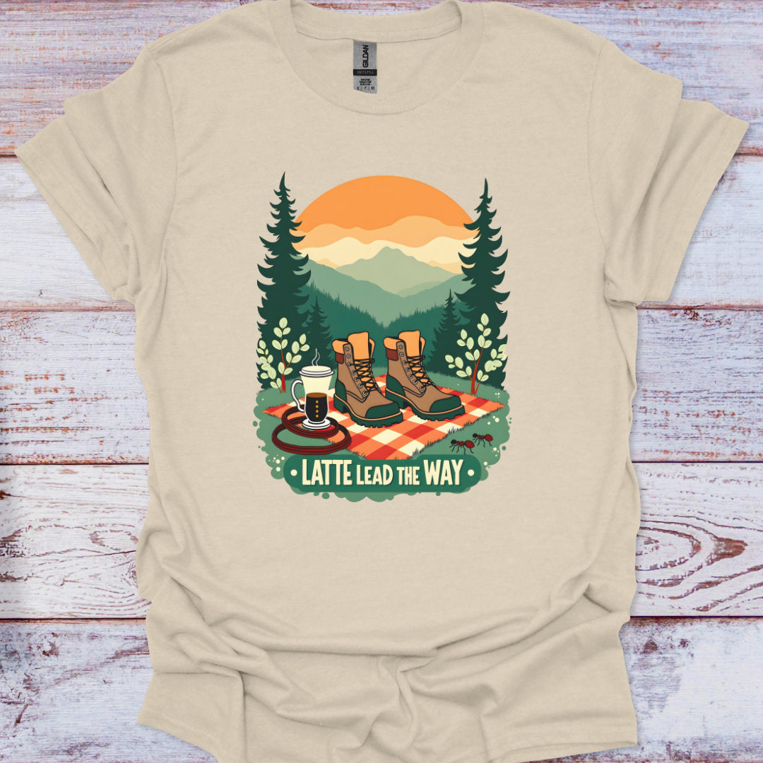 Beige t-shirt with a graphic of hiking boots, coffee, and trees on a wooden surface