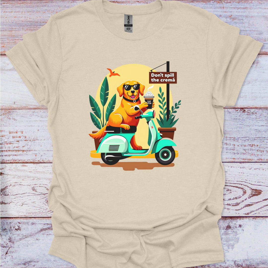Beige t-shirt with a colorful graphic of a dog on a scooter and text 'Don't spill the crema' on a wooden surface.
