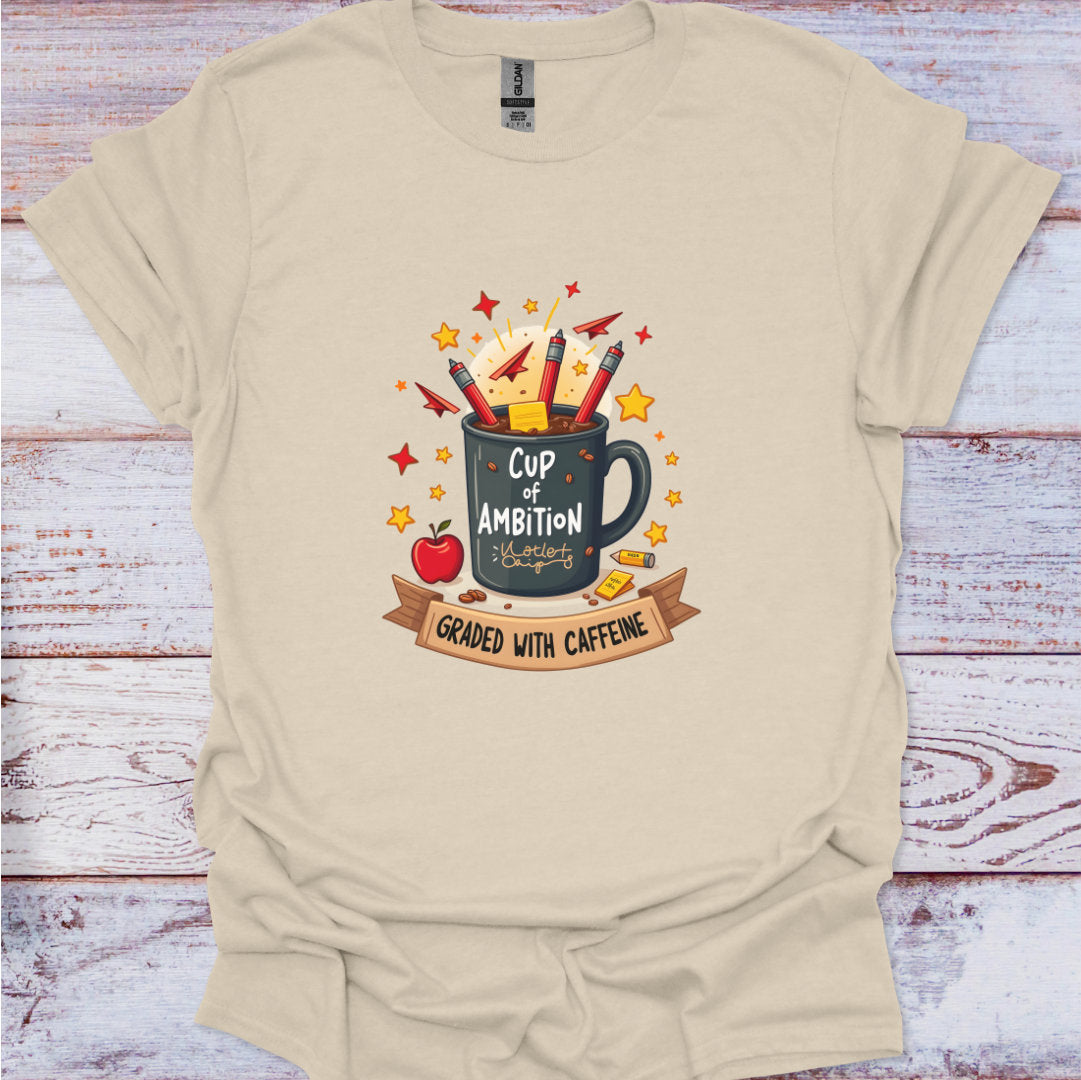 Beige t-shirt with a graphic design of a mug labeled 'Cup of Ambition' on a wooden surface.