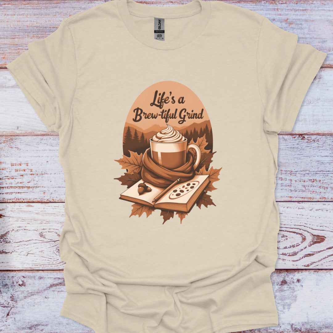 Beige t-shirt with a coffee-themed graphic and 'Life's a Brew-tiful Grind' text on a wooden surface.