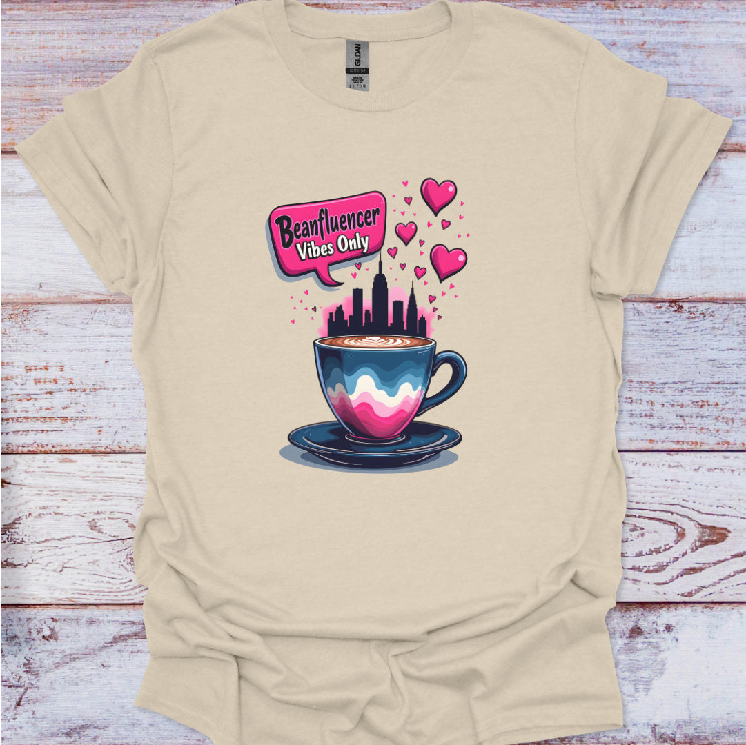 Beige t-shirt with a colorful graphic of a coffee cup and cityscape on a wooden surface