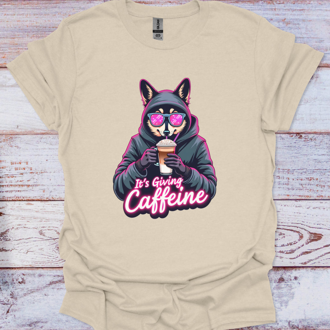 Beige t-shirt with a graphic of a fox in a hoodie holding a coffee cup and text 'It's Giving Caffeine' on a wooden surface.