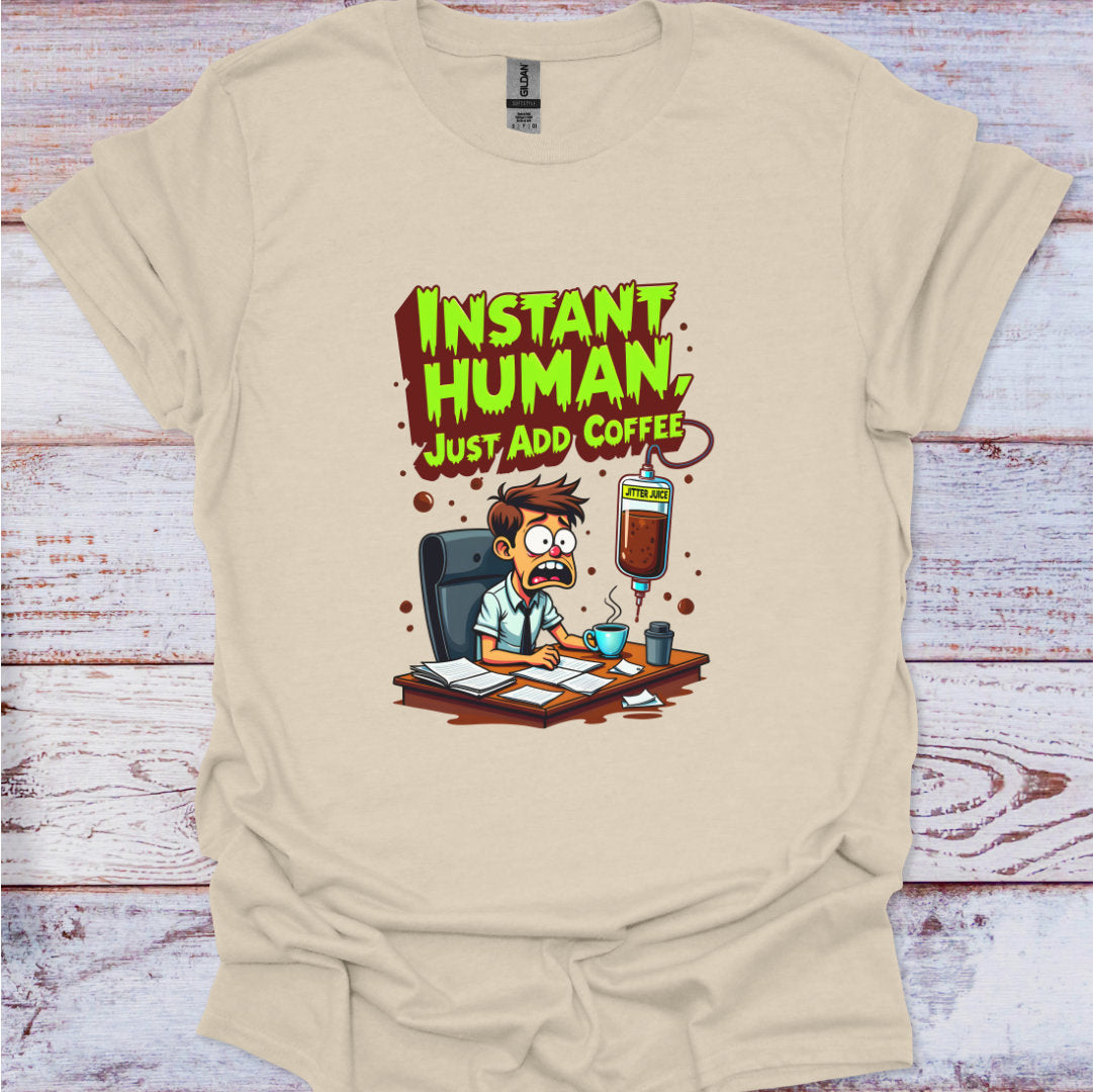 Beige t-shirt with a cartoon character and text 'Instant Human, Just Add Coffee' on a wooden surface.
